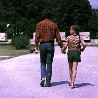 Man and child walk hand-in-hand along a paved path.