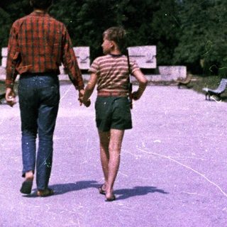 Man and child walk hand-in-hand along a paved path.