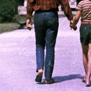 Man and child walk hand-in-hand along a paved path.
