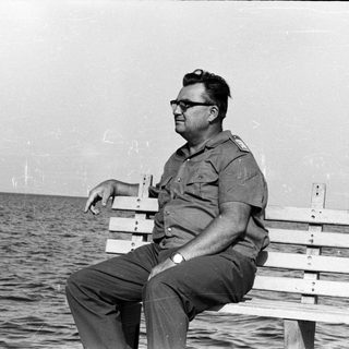 Man in uniform sits on a bench by the sea.