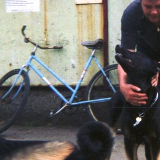 Man holding a dog near a building and bicycle.