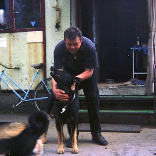 Man holding a dog near a building and bicycle.