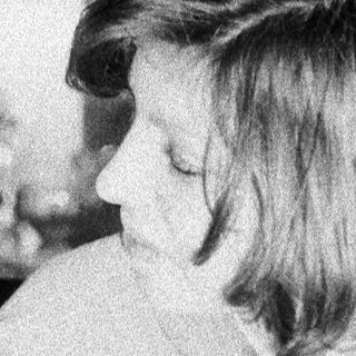 Here's a brief summary of the image: Young girl sits pensively in a kitchen setting.