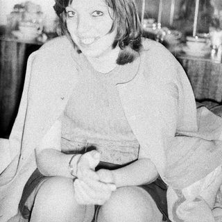 Here's a brief summary of the image: Woman seated, looking at camera, with kitchenware in background.