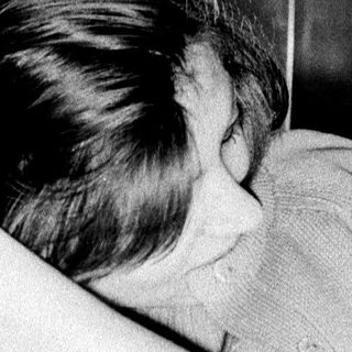 Here's a brief summary of the image: Woman seated, head down, appearing distressed in a room.