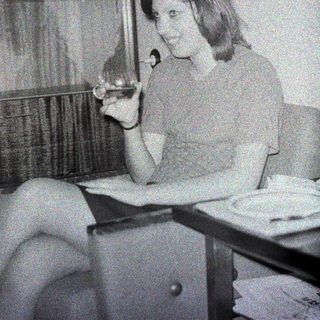 Here's a brief summary of the image: Woman seated, holding a cigarette, in a vintage setting.