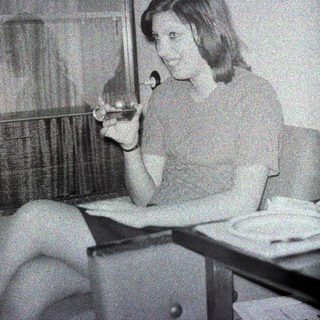 Here's a brief summary of the image: Woman seated, holding a cigarette, in a vintage setting.