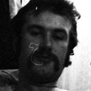 Couple relaxing in bed, man smoking, guitar nearby.