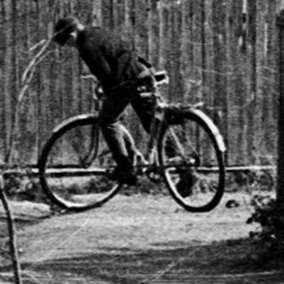 Bicycle leaning against a fence along a dirt road.