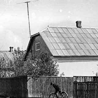 Bicycle leaning against a fence along a dirt road.