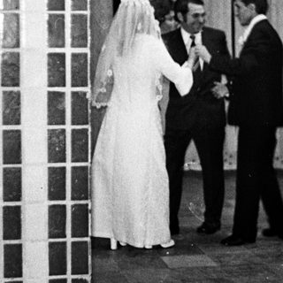 Couple in wedding attire stands near a brick wall.