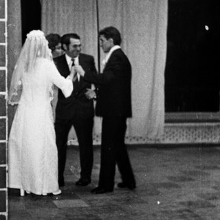 Couple in wedding attire stands near a brick wall.