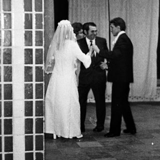Couple in wedding attire stands near a brick wall.
