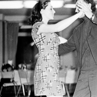 Couple dancing in a room with tables and chairs.