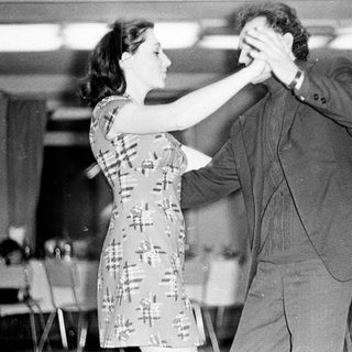 Couple dancing in a room with tables and chairs.