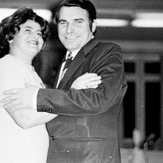 Couple embraces in a formal, black and white portrait.
