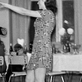 Couple dances in a room with tables and chairs.