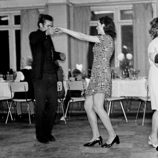 Couple dances in a room with tables and chairs.