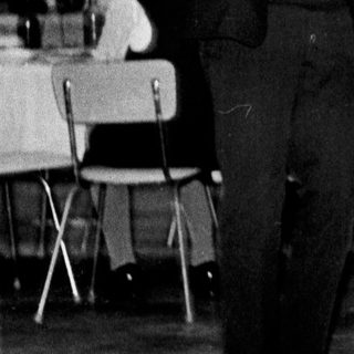 Couple dances in a room with tables and chairs.