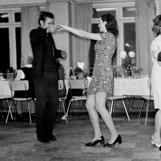 Couple dances in a room with tables and chairs.