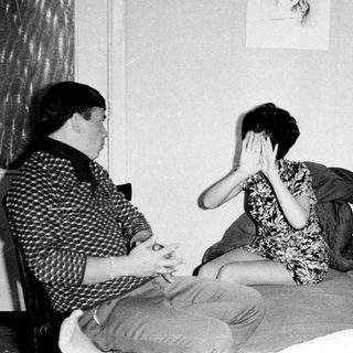 Three people seated on a bed in a room.