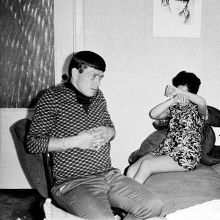 Three young people seated in a sparsely furnished room.
