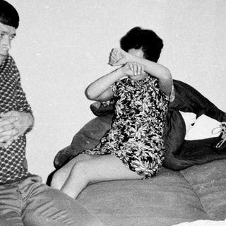 Three young people seated in a sparsely furnished room.