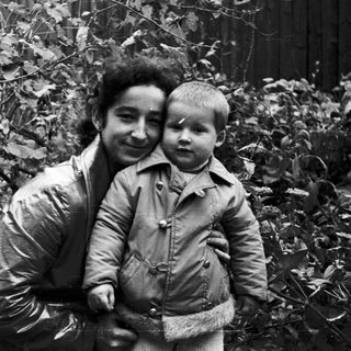 Woman holding a child in a wooded area.