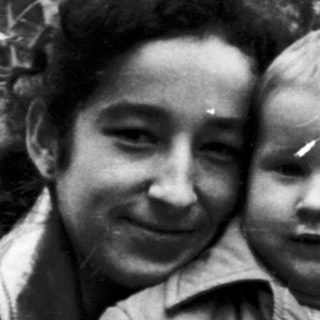 Woman holding a child in a wooded area.