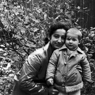 Woman holding a child in a wooded area.