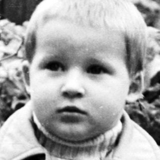 Black and white photo of a young boy near foliage.