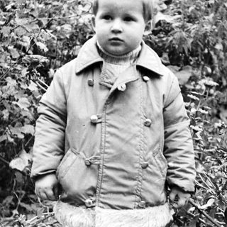 Black and white photo of a young boy near foliage.