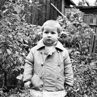 Black and white photo of a young boy near foliage.