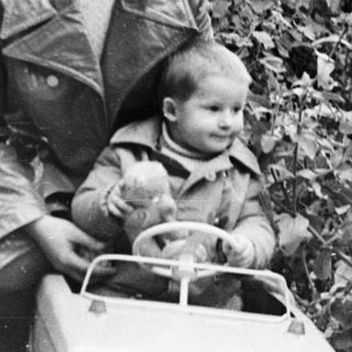 Woman and child sit on toy car near a fence.