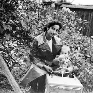 Man and child seated in a toy car outdoors.