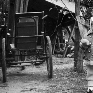 Child and adult stand near a building and toys.
