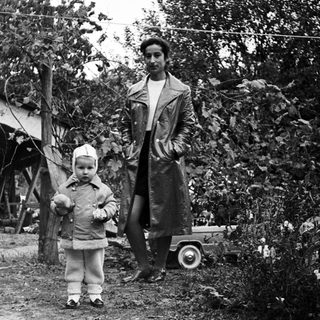Child and adult stand near a building and toys.