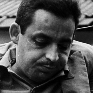 Man in jacket stands near railing, looking downward.