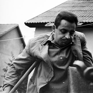 Man in jacket stands near railing, looking downward.