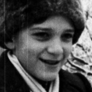 Young person in winter coat and hat, standing near a fence.