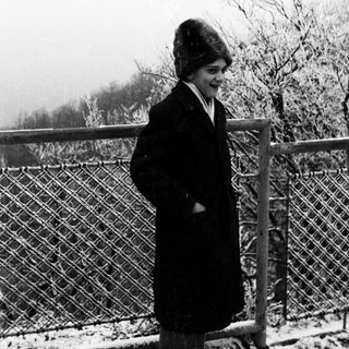 Here's a brief summary of the image: Woman in coat stands near a snowy fence.