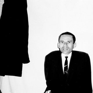 Man in suit stands against a wall with bookshelves.