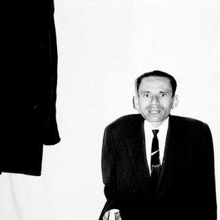 Man in suit stands against a wall with bookshelves.