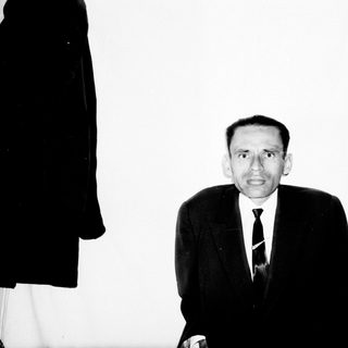 Man in suit stands near a bookshelf, black and white photo.