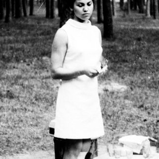 Woman stands near tree stumps in a wooded area.