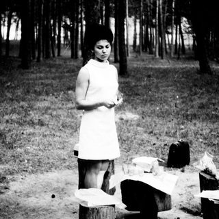 Woman stands near tree stumps in a wooded area.