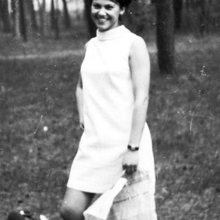 Woman in dress stands in a wooded area.