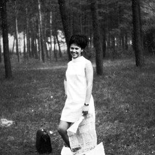 Woman in dress stands in a wooded area.