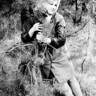 Woman seated outdoors, holding pine needles, in a grassy area.
