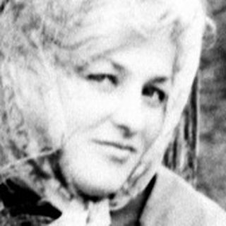 Woman seated outdoors, holding pine needles, in a grassy area.
